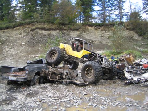 1990 Ford Bronco - An off-road buggy is perched precariously on a heavily damaged pickup truck, surrounded by debris in a challenging terrain.