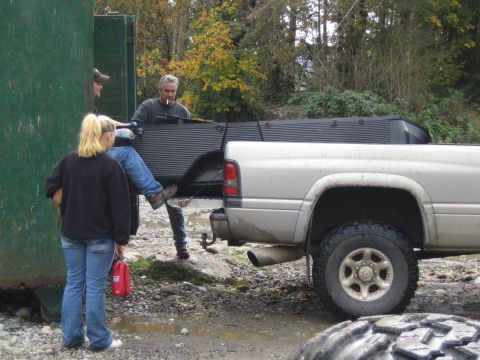 1990 Ford Bronco - A silver pickup truck's rear quarter panel and bed are visible as people load items into a large green container.