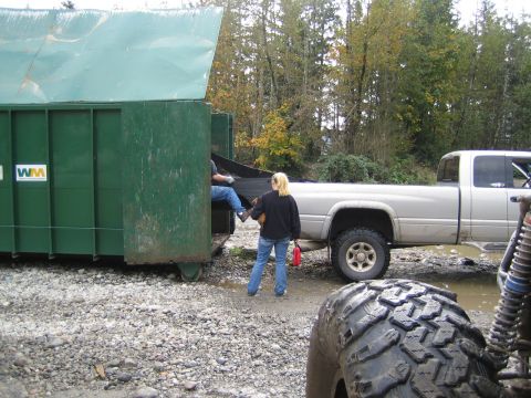 1990 Ford Bronco - People loading a dumpster next to a silver pickup truck. A tire from another vehicle is visible.