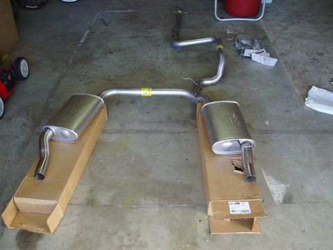 1993 Ford Taurus - New dual exhaust system components laid out on cardboard boxes in a garage.
