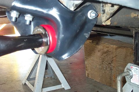 1995 Ford Bronco - Underside view of a freshly painted black radius arm mounted in its frame bracket with a new red polyurethane bushing and washer at the piv…