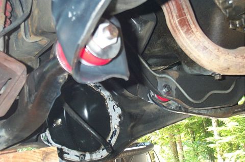 1995 Ford Bronco - Underside view of a Ford Bronco showing the front differential cover, a red-bodied shock absorber with a large hex bolt, and a coil spring,…