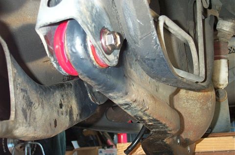 1995 Ford Bronco - Close underside view of a newly installed red polyurethane sway-bar bushing clamped in its bracket against the frame, with the fresh bolt a…