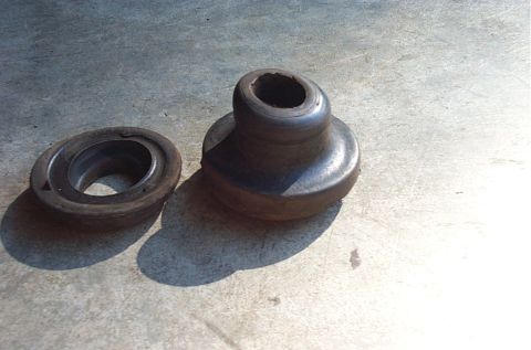 1995 Ford Bronco - Two old rubber radius arm bushing halves lying on a concrete garage floor after removal, the taller cone-shaped piece cracked and distorted…