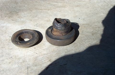 1995 Ford Bronco - Two worn rubber suspension bushings on a sunlit concrete floor, the right-hand one molded with "LEFT HAND" text and a part number and badly…