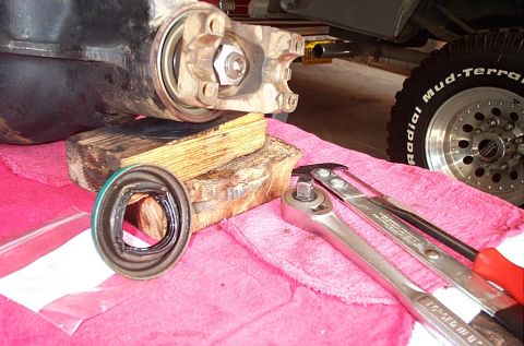 1995 Ford Bronco - Close-up of a pinion seal replacement: the removed differential housing rests on wood blocks with the pinion yoke and nut visible, while a…