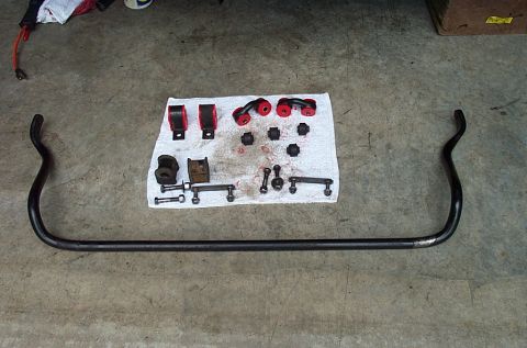 1995 Ford Bronco - A bare steel anti-sway bar lies on a garage floor with its hardware laid out above it on a white towel: red polyurethane bushings, black ru…
