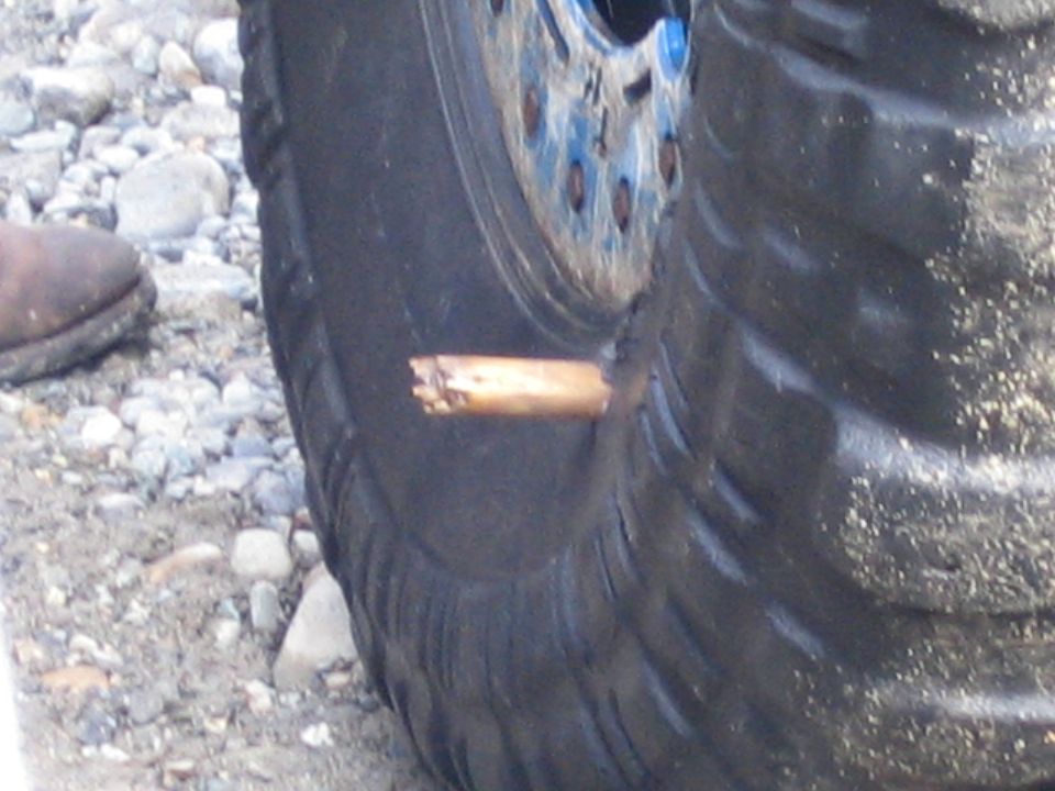 Close-up of a tire with a wooden object stuck in it. A person's boot is visible to the left