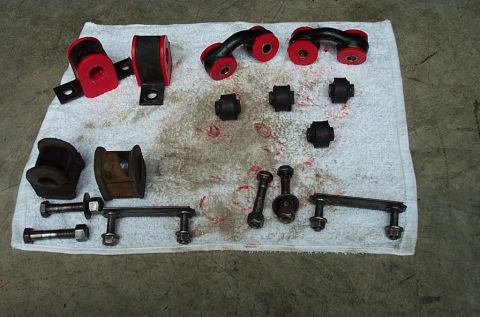 1995 Ford Bronco - Close overhead view of sway-bar hardware arranged on a greasy white shop towel: red polyurethane bushings pressed into brackets and forged…