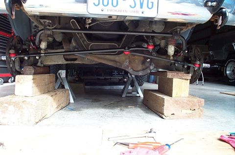 1995 Ford Bronco - Low front view under a lifted truck on jack stands and wood cribbing, showing the Dana front axle housing, coil-spring/radius-arm suspensio…
