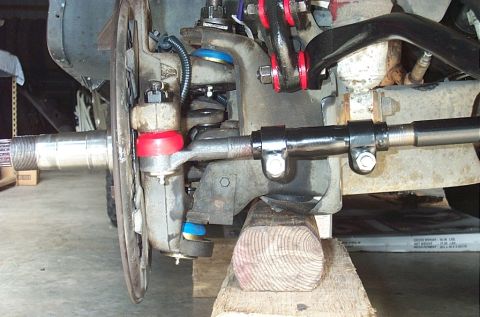 1995 Ford Bronco - Close-up of a solid front axle and steering assembly on a 4x4, resting on a wooden block. It shows the knuckle and splined stub, brake back…