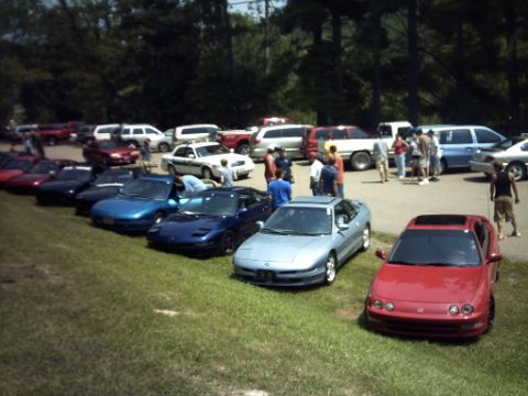 1995 Ford Probe - A gathering of vehicles, several sports cars lined up on a grassy area with trees in the background.