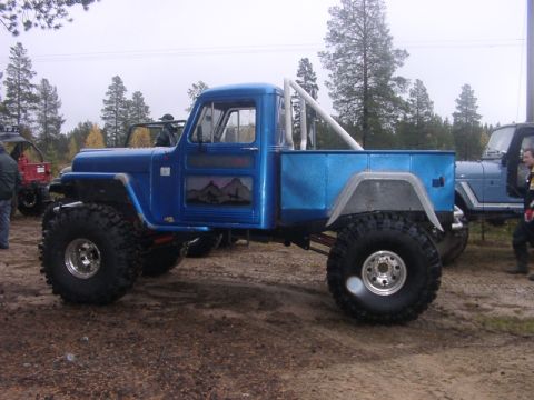 1981 Ford Bronco - A heavily modified blue pickup truck with oversized tires and a custom mountain mural on the driver's door is parked outdoors.