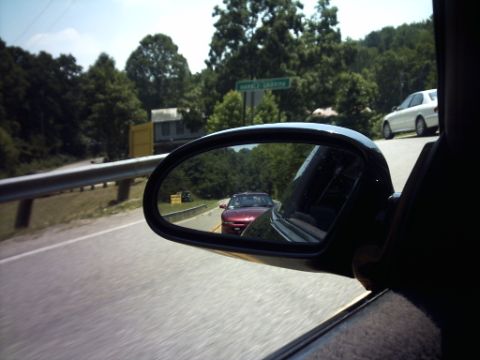 1995 Ford Probe - View from driver's side mirror shows a red car following, with a white car visible further ahead on the road.