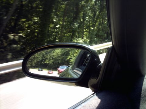 1995 Ford Probe - Three cars are visible in the side mirror of a vehicle driving on a tree-lined road.