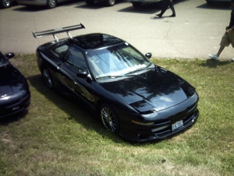 1995 Ford Probe - A black 1995 Ford Probe is parked on the grass with a large rear spoiler and custom wheels.
