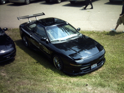 Black 1995 Ford Probe with a big wing and custom wheels parked on grass next to another car