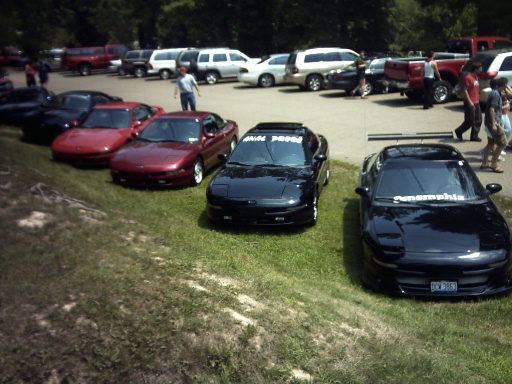 Three black Ford Probes and two red Ford Probes parked on grass and asphalt