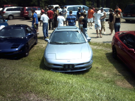 1995 Ford Probe parked on grass, front view. Blue car to the left, red car to the right. People gathered in the background