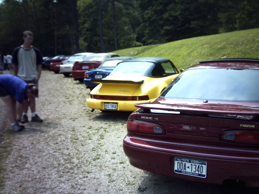 Maroon Mazda MX-6 rear view with license plate DDA-1340 and yellow Porsche 911 in background