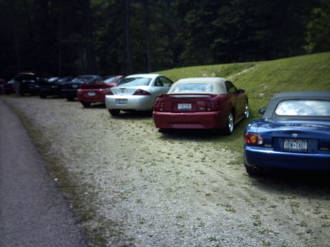 1995 Ford Probe - Rear view of a red convertible Mustang parked in a line of cars.