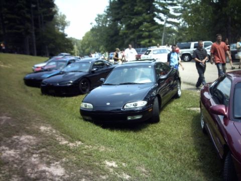 1995 Ford Probe - Multiple vehicles are parked on a grassy area, with trees lining the background.