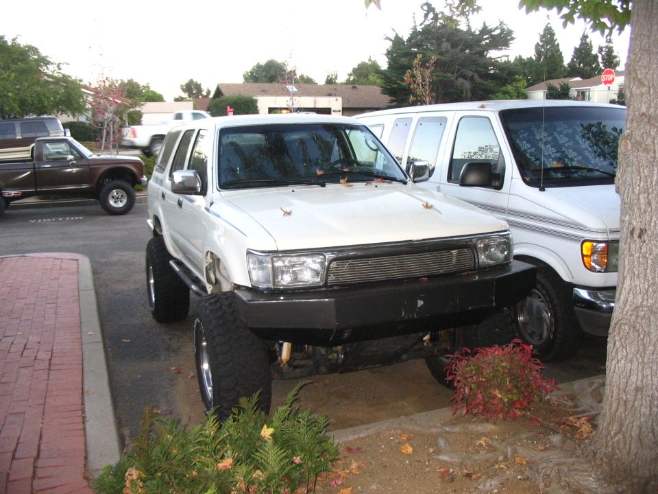 White lifted Toyota 4Runner with custom front bumper parked in a driveway by houses