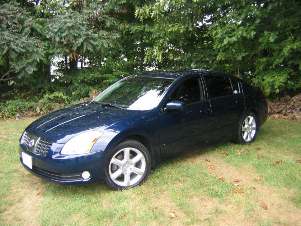 Dark blue Nissan Maxima sedan parked on grass, front three-quarter view