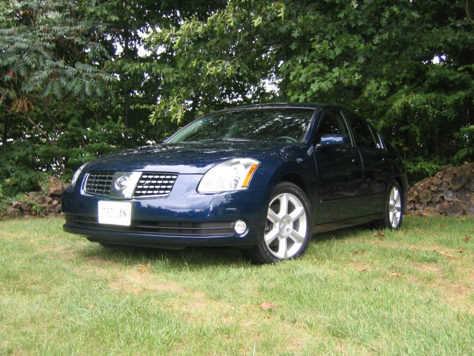 Dark blue Nissan Maxima sedan parked on grass, front three-quarter view
