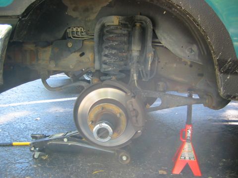 1996 Ford Bronco - Front suspension of a teal truck with the wheel removed, showing the coil spring, shock absorber, radius arm, brake rotor, caliper and 5-lu…