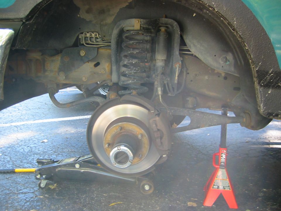 Front coil-spring suspension and brake rotor with wheel off, on red jack stand