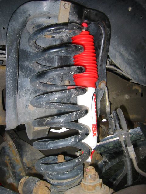 1996 Ford Bronco - Newly installed white Rancho RSX shock with a red boot mounted inside the front coil spring of a truck, shot from under the fender well. Th…