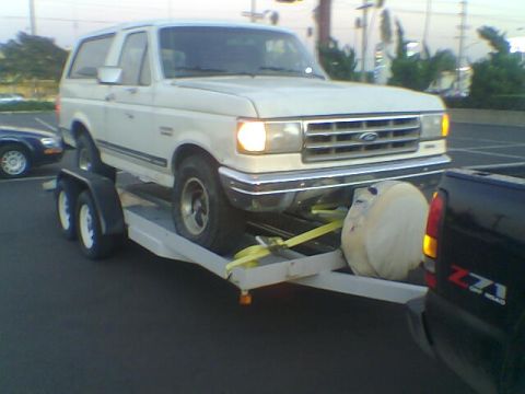 1988 Ford Bronco - White Ford Bronco loaded onto a trailer, with a black truck visible on the right.