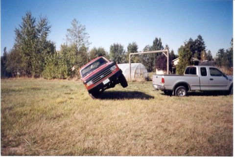 1989 Ford Bronco - A red pickup truck appears stuck in a field next to a silver pickup truck.