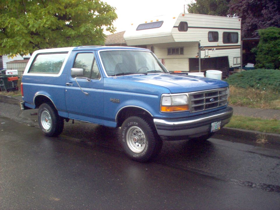 Blue 1992 Ford Bronco parked on wet street, 3q-front view