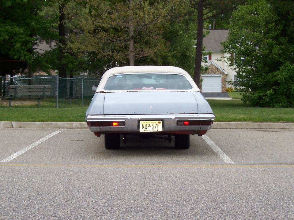 Rear view of a light blue convertible parked in a lot. It has a white top and a license plate that reads NUP-57F