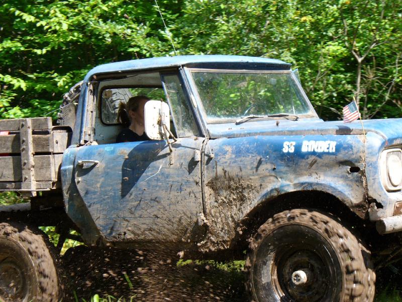Muddy blue International Scout 800 driving through mud with off-road tires spraying dirt