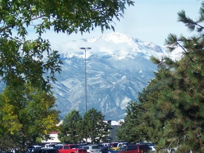 1972 Ford Ranchero - A parking lot is visible in the foreground, with trees framing a view of snow-capped mountains under a partly cloudy sky.