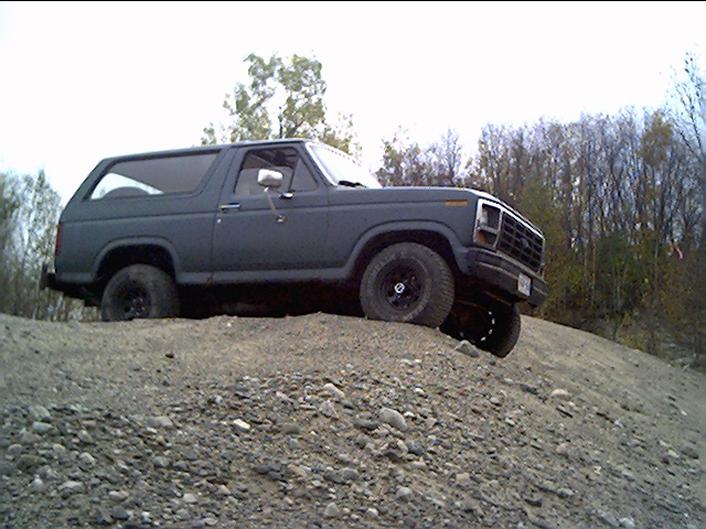 Dark gray Ford Bronco climbing a dirt hill. Black wheels, off-road tires