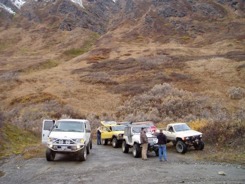 2000 Ford E350 - A convoy of off-road vehicles, including a white van and several Jeeps, are parked on a gravel road with a mountainous backdrop.