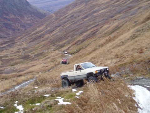 2000 Ford E350 - Multiple off-road vehicles traverse a challenging mountain path in a scenic, landscape.