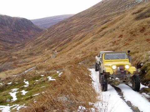 2000 Ford E350 - A yellow Jeep CJ-7 navigates a snowy and muddy mountain trail, its off-road capabilities.