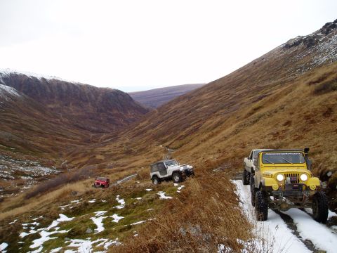 2000 Ford E350 - Three off-road vehicles navigate a snowy mountain trail in a valley.