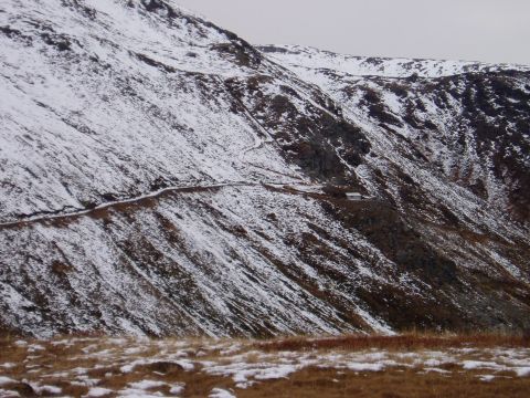 2000 Ford E350 - A remote mountain pass is covered in snow, with a narrow road winding up the slope towards a small structure.