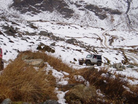 2000 Ford E350 - Two off-road vehicles navigate a snowy mountain path with rocky terrain.
