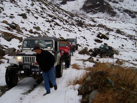 2000 Ford E350 - A group of Jeeps navigates a snowy, mountainous terrain, with one person walking alongside the lead vehicle.