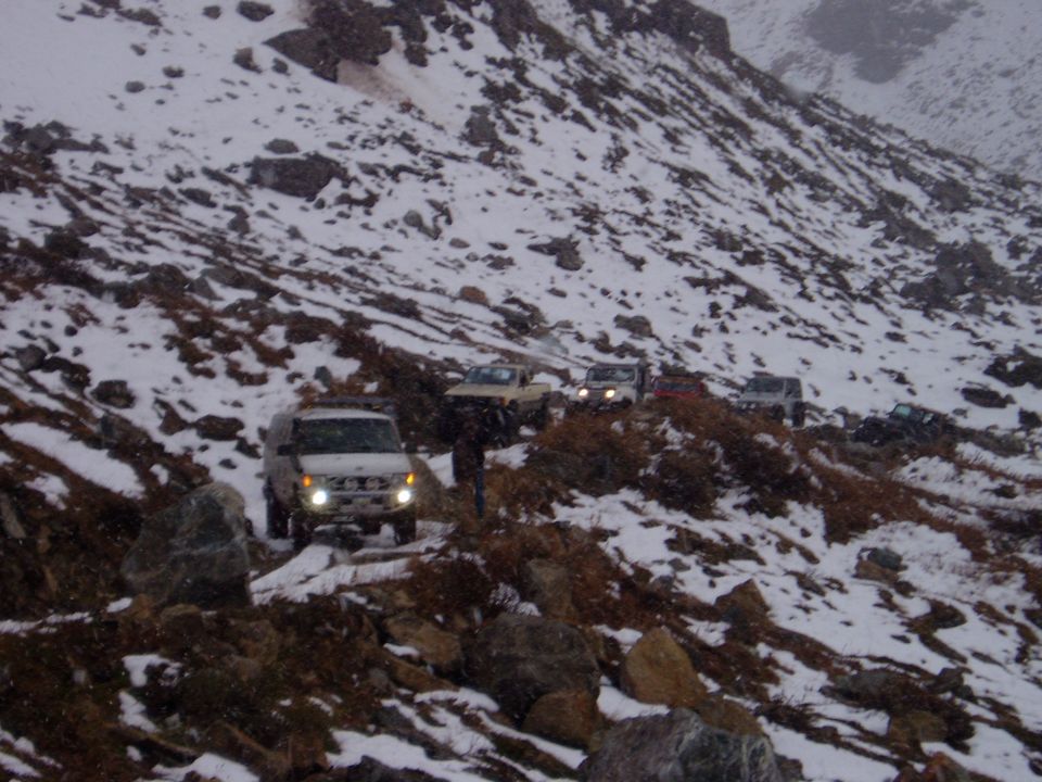 White SUV with headlights on driving on a rocky, snow-covered mountain path