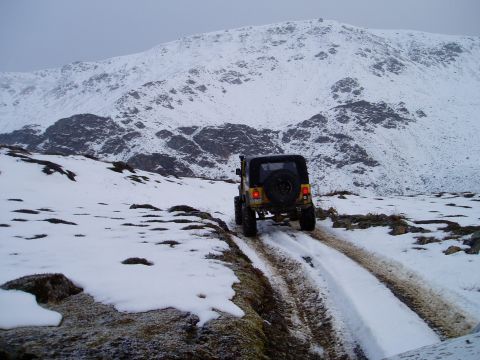 2000 Ford E350 - A yellow Jeep Wrangler navigates a snow-covered mountain trail, kicking up mud and snow.