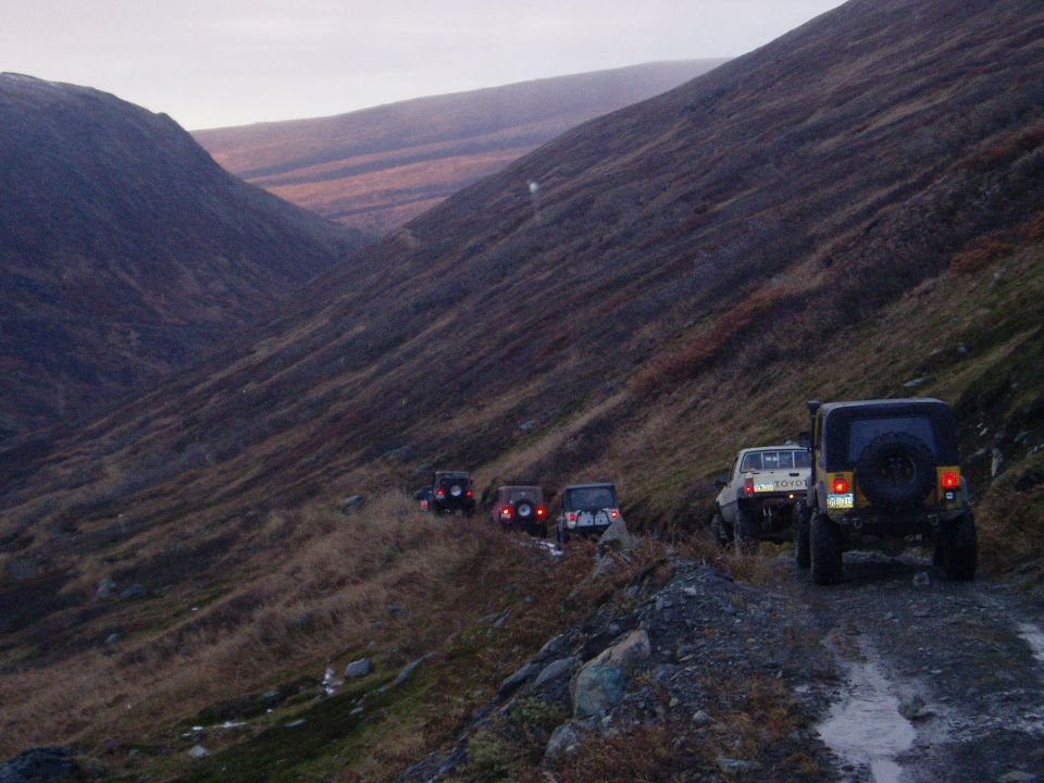 Several off-road vehicles driving on a dirt road through a mountain valley