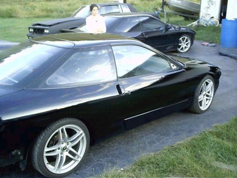 1994 Ford Probe - A black coupe is parked next to another black car, with a woman visible through the sunroof.